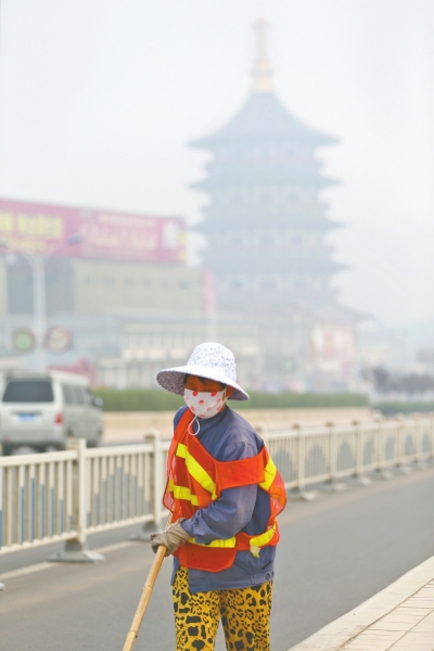 近日，在古都洛陽(yáng)，環(huán)衛(wèi)工人身后的“天堂”被霧霾籠罩著。