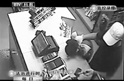戴帽男子一手掐住加油站營(yíng)業(yè)員，一手持發(fā)令槍指向另一營(yíng)業(yè)員，要求“把錢給我裝起來(lái)”。