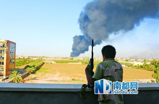 2日，利比亞首都的黎波里，一民兵武裝成員眺望被火箭彈擊中的儲油罐冒出濃煙。