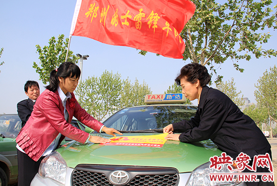 　　授旗結(jié)束后，首都的士雷鋒車隊(duì)王鳳進(jìn)隊(duì)長(zhǎng)（右）與鄭州的的哥的姐在車身上貼上標(biāo)識(shí)。