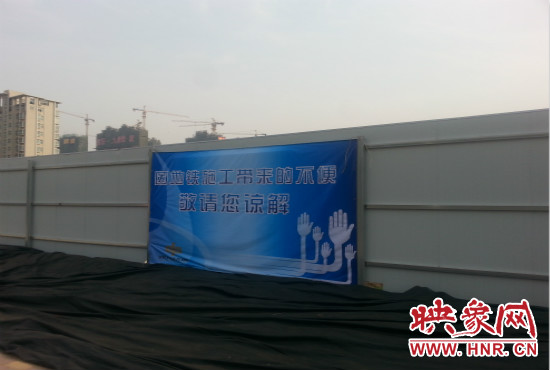 道路南側(cè)圍起了白色的圍擋，墻上標(biāo)示著“因地鐵施工帶來(lái)的不便敬請(qǐng)您諒解”的提示牌。