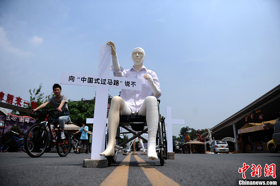 4月16日，重慶市洋人街上擺放著兩個受了傷的塑料人像“模特”，旁邊十字架上寫著向“中國式過馬路”說不