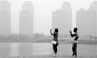 29日中午，鄭東新區(qū)如意湖畔，兩個(gè)年輕人拍攝霧霾中的景色。 鄭州晚報(bào)記者 馬健 圖