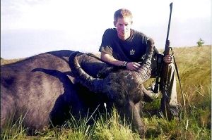 哈里王子手持獵槍，蹲在一頭遭到獵殺的水牛旁邊