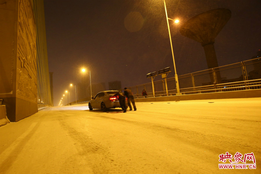 雪天路滑，汽車上橋打滑，兩名“推車人”幫助一輛私家車上坡。