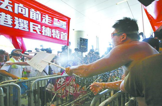 17日，在香港立法會外，一名反對政改的男子向支持派人群投擲標牌。
