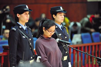 被告人盧梅低著頭，站在朝陽法院刑事審判庭的被告席上。